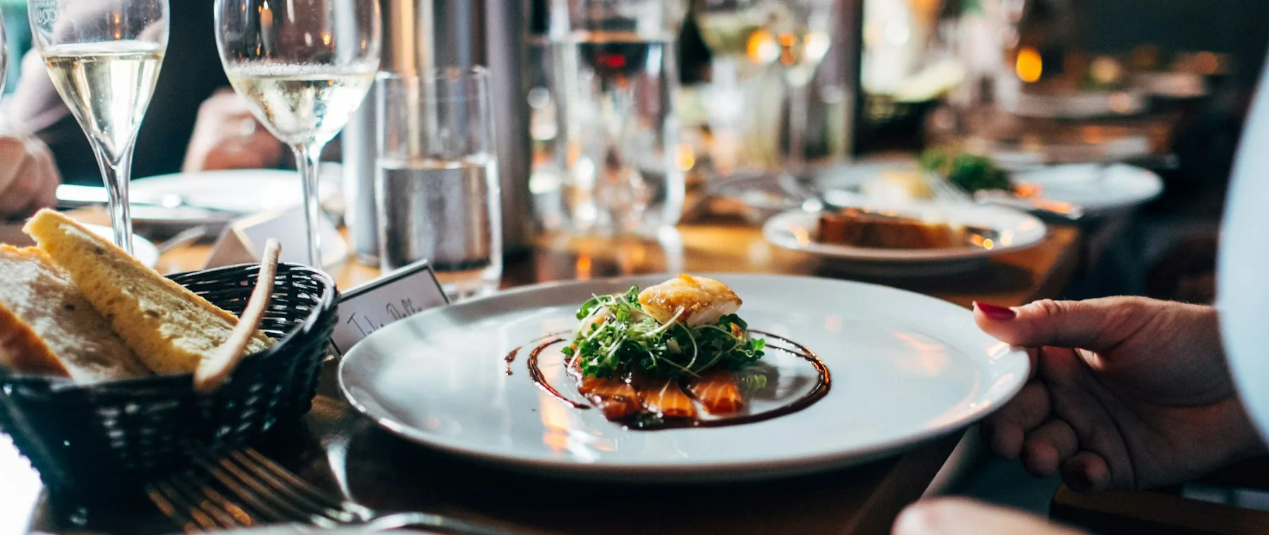 A server placing a plated main course on a table during dinner service.