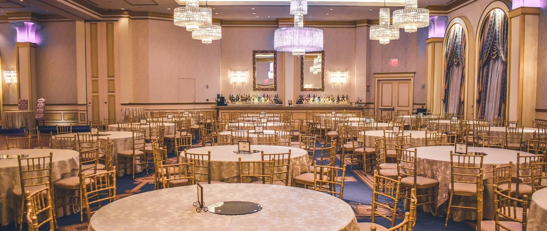 A hotel ballroom set with round tables and chiavari chairs before a reception.