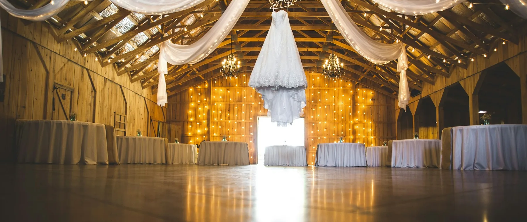 A warmly lit barn venue set up with tables before a reception.