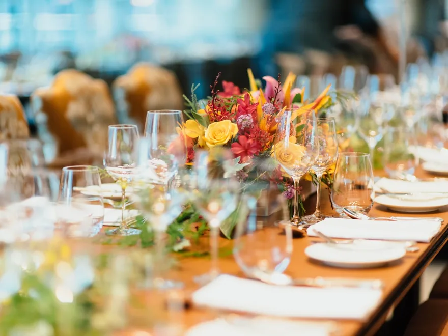 A long event table styled with warm florals, candles and glassware.