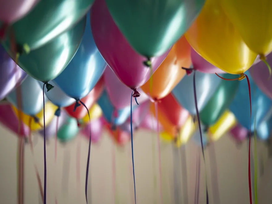 A cluster of pastel balloons floating against a bright ceiling.