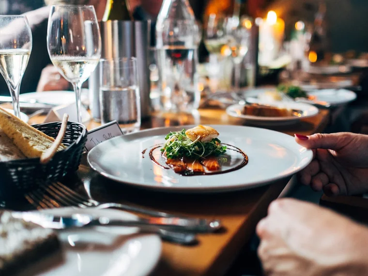 A server placing a plated main course on a table during dinner service.