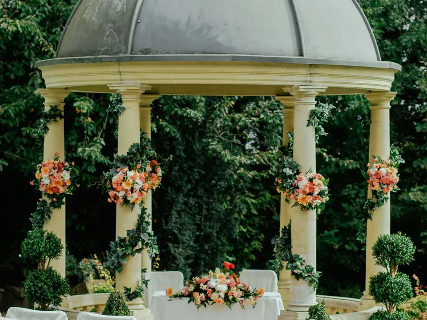 A white canopy structure decorated with florals at an outdoor ceremony.